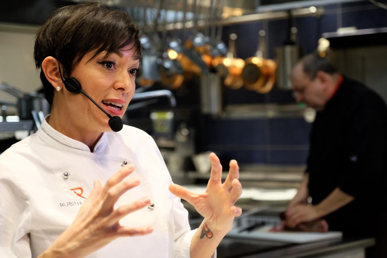 Rubina Rovini racconta la ricetta al pubblico mentre la brigata lavora alle sue spalle.