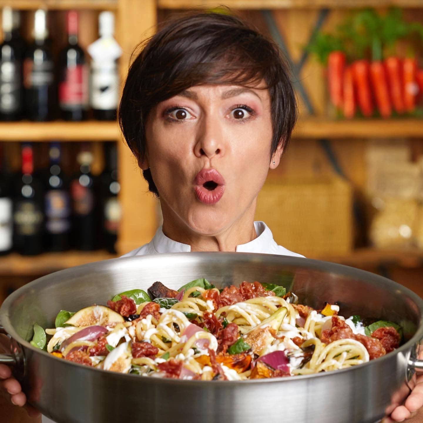 Rubina Rovini con l'espressione stupita mentre solleva una padella di spaghetti sul set de La Versione di Rubi.