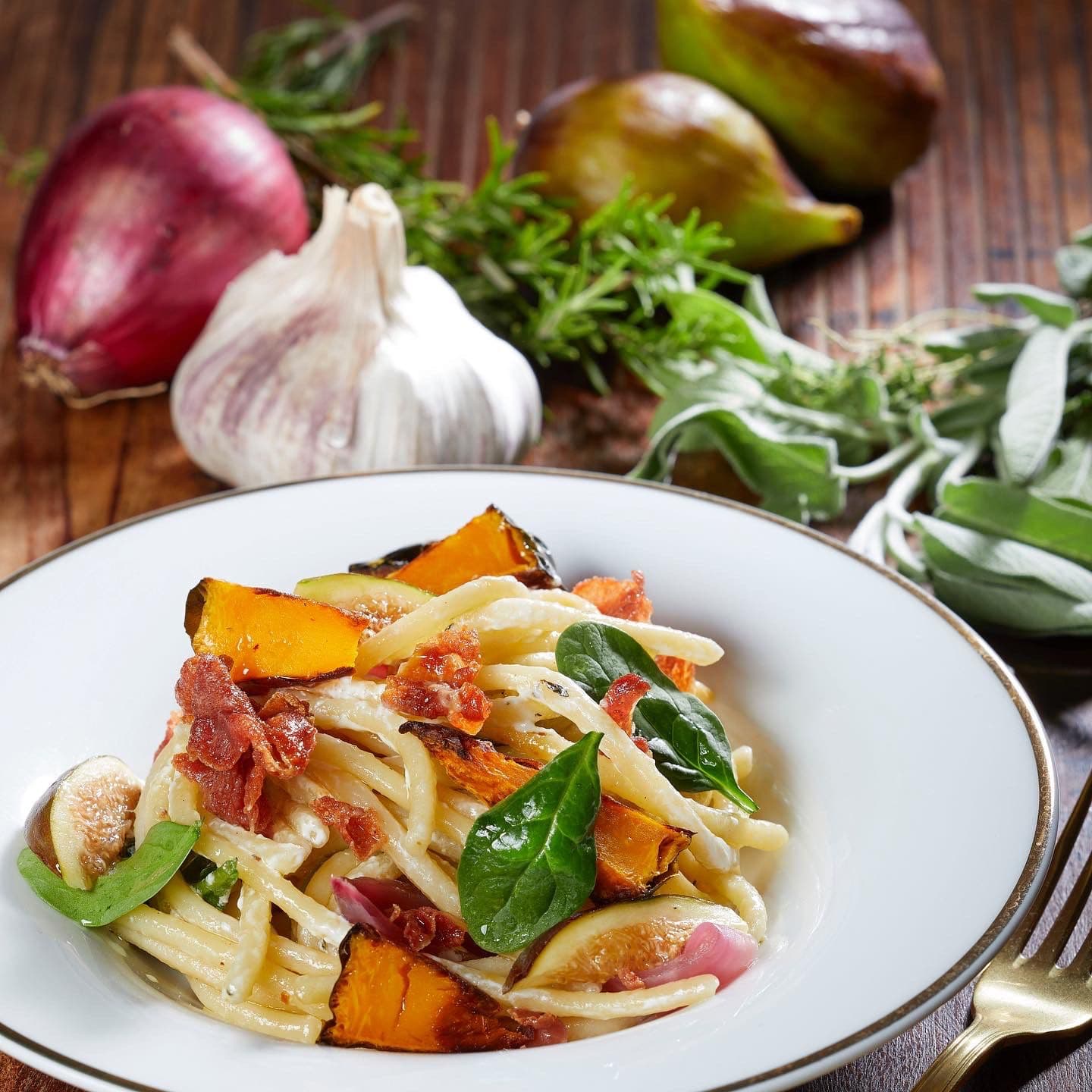 Pasta con zucca e fichi servita nel piatto, con gli ingredienti freschi accanto.