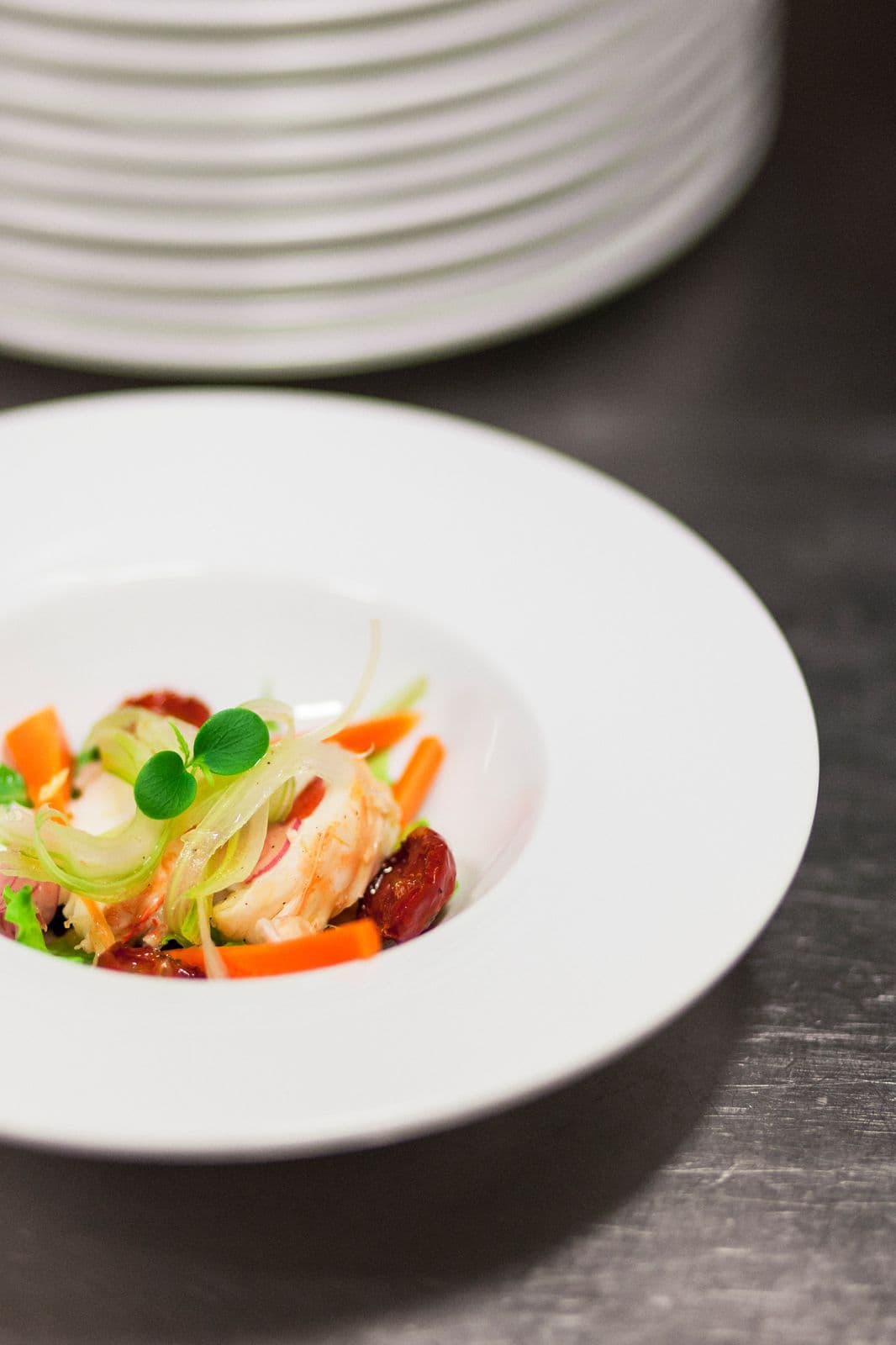 Piatto di crudo e verdure impiattato sopra una pila di piatti bianchi.