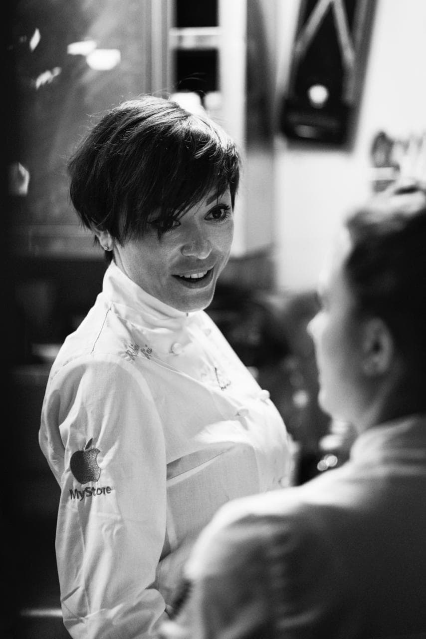 Rubina Rovini in giacca bianca parla con un collega durante il servizio.
