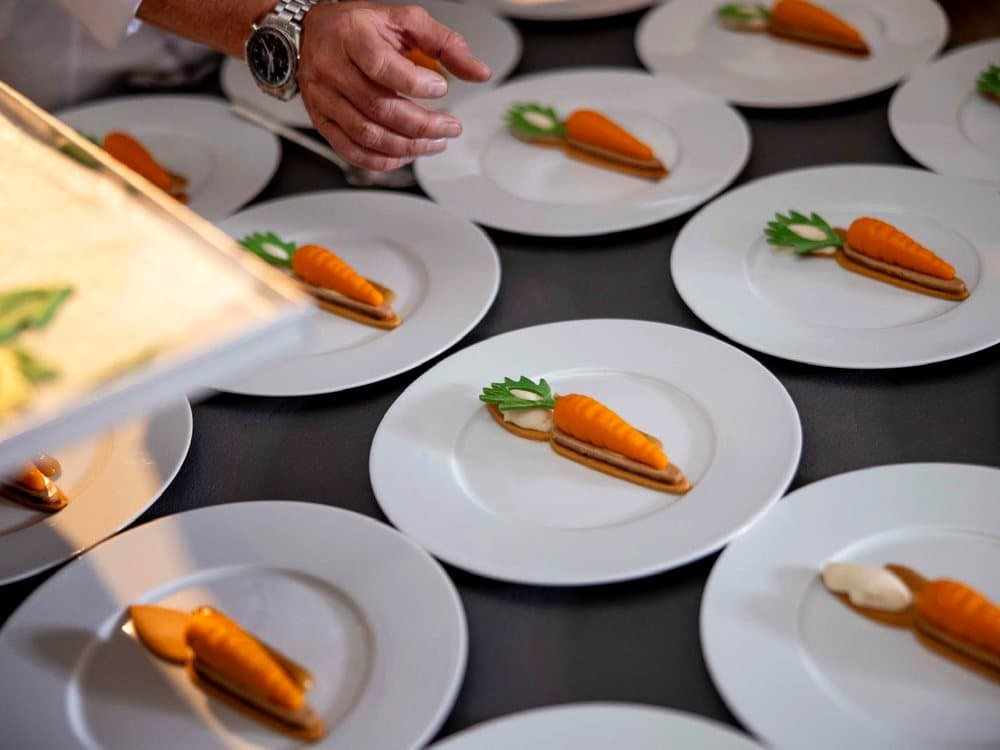 Il dessert a forma di carota impiattato in serie sui piatti bianchi, pronto per il servizio a Chefs for Life.