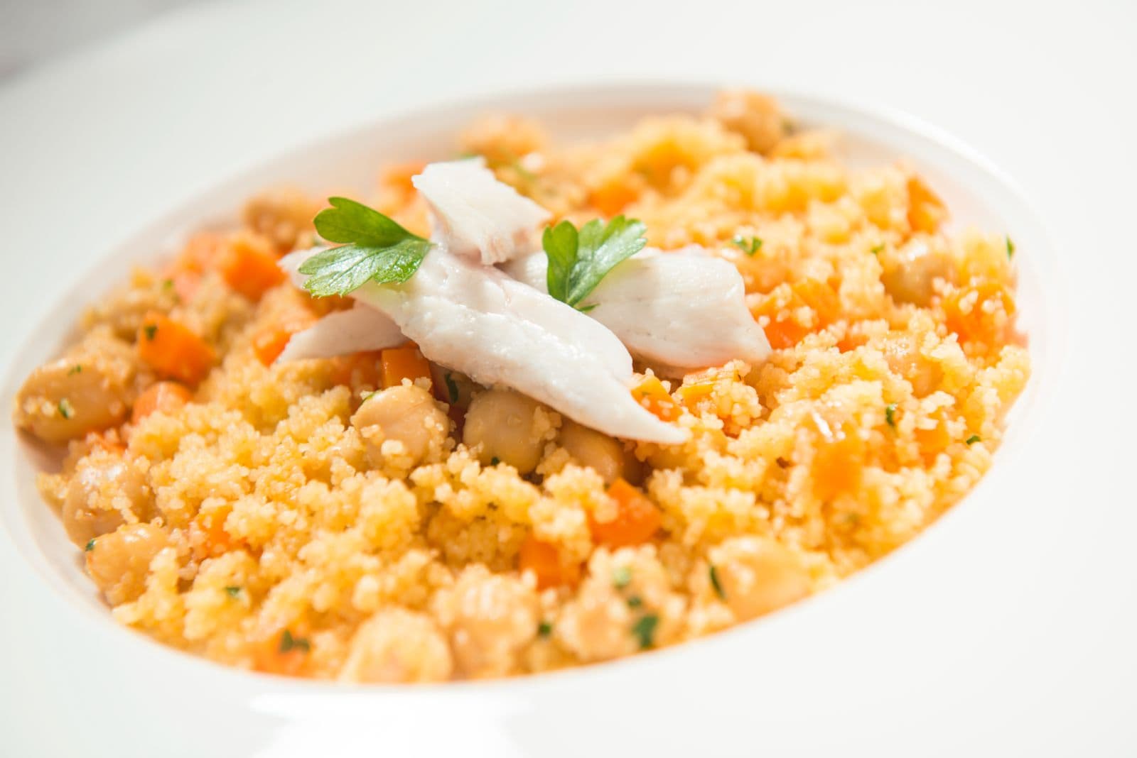 Cous cous con pesce e verdure servito nel piatto bianco.