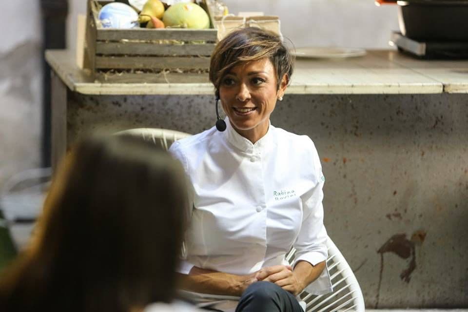 Rubina Rovini seduta durante un'intervista in fiera, con le cassette di frutta alle spalle.
