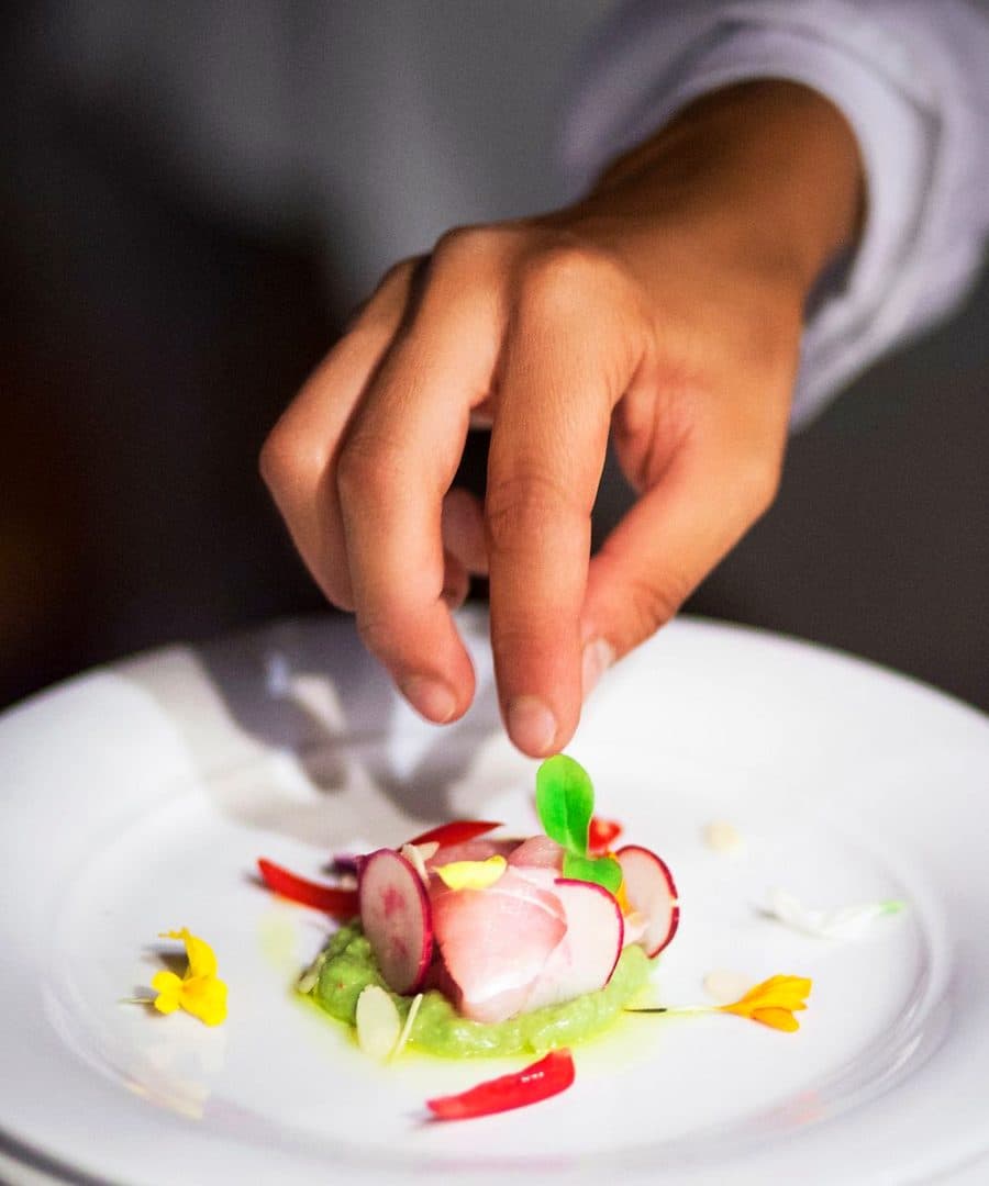 Le mani di Rubina Rovini completano un crudo di pesce con ravanelli e fiori commestibili.