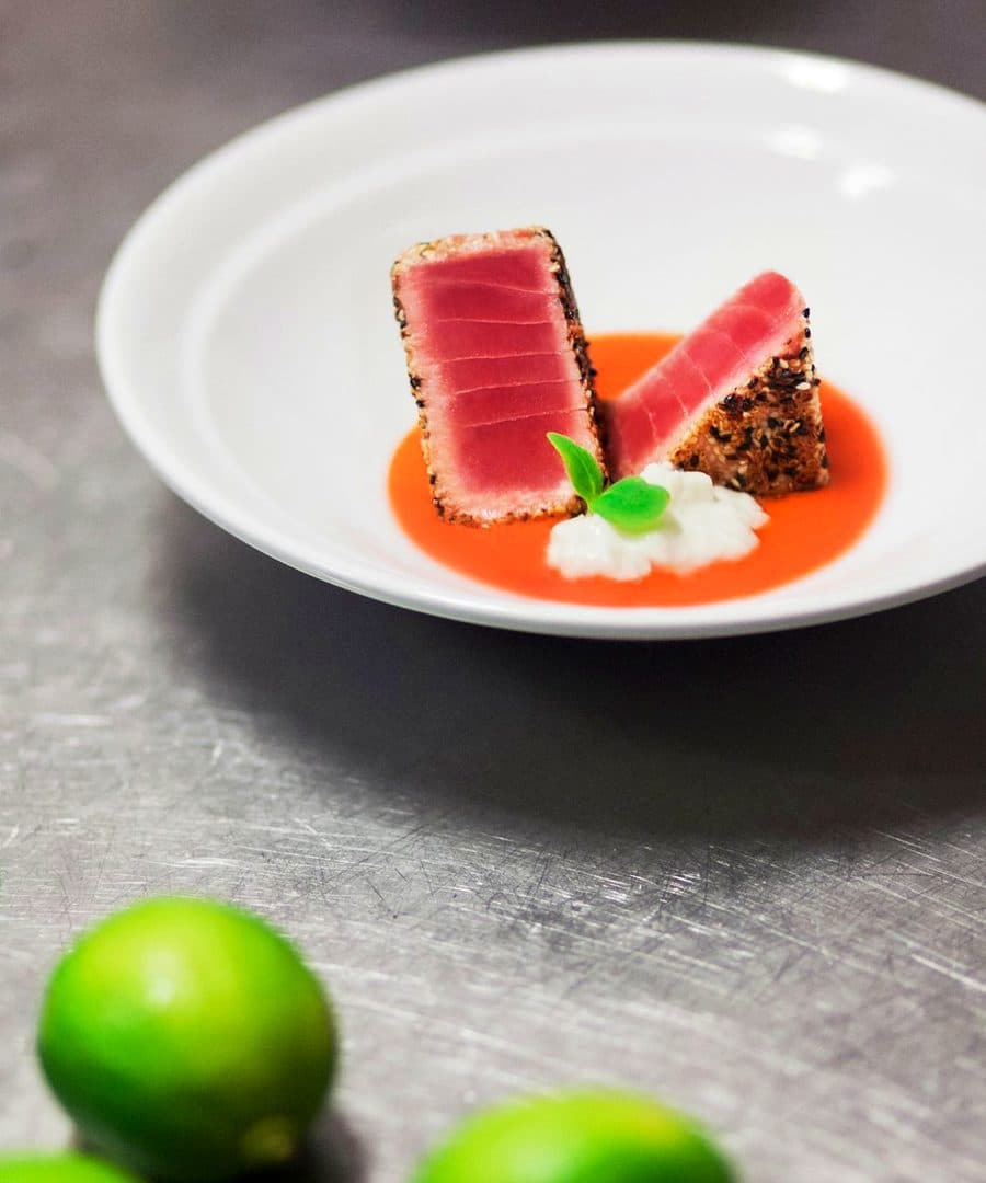 Tonno scottato in crosta di semi con salsa al pomodoro e lime interi accanto al piatto.
