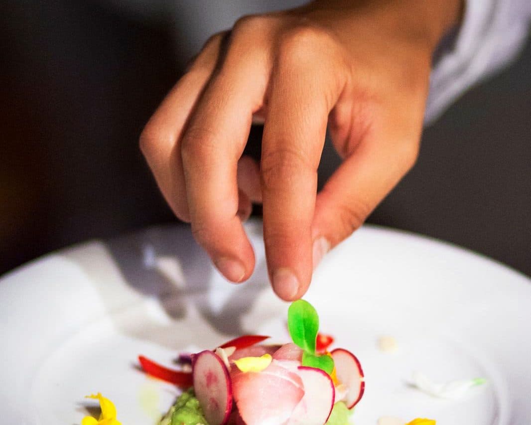 Le mani di Rubina Rovini completano un crudo di pesce con ravanelli e fiori commestibili.