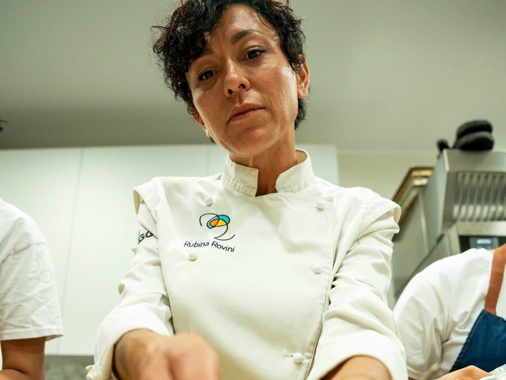Rubina Rovini in giacca da cuoco al lavoro nella cucina professionale di RADICI Lab.